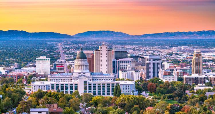 Sonnenuntergang-Panorama von Salt Lake City mit dem Utah State Capitol vor farbenfrohem Himmel und entfernten Gipfeln.