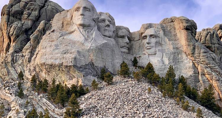 Caras de granito del Monte Rushmore talladas en un acantilado escarpado with pinos abajo.