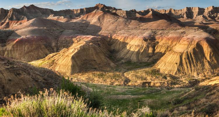Crestas y barrancos erosionados y coloridos del Parque Nacional Badlands iluminados por el cálido sol de la tarde.