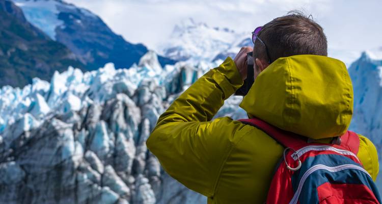 Homme en veste verte photographie la glace bleue dentelée du glacier Perito Moreno avec des sommets enneigés en arrière-plan.
