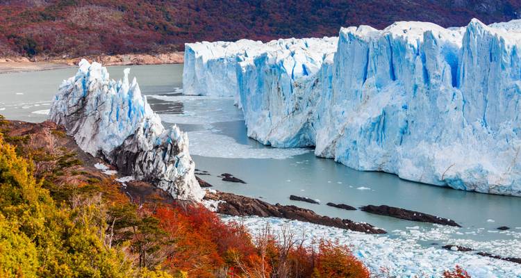 Vue panoramique de parois glaciaires déchiquetées rencontrant une rivière laiteuse au milieu d'une forêt automnale éclatante.