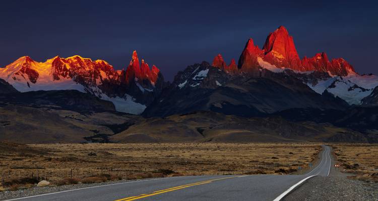Une route désertique mène vers la chaîne du Fitz Roy qui rougeoie dans la lumière dramatique du coucher de soleil.