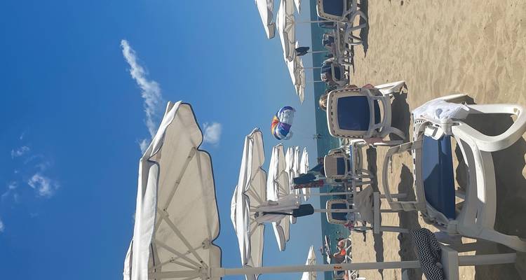 Rows of sun-loungers and parasols line a sunny sandy beach with a colorful parasail overhead in Varna.