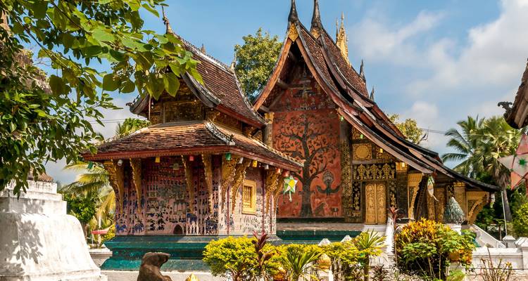 Der reich verzierte Wat Xieng Thong Tempel erstrahlt inmitten tropischer Vegetation unter blauem Himmel in Luang Prabang.