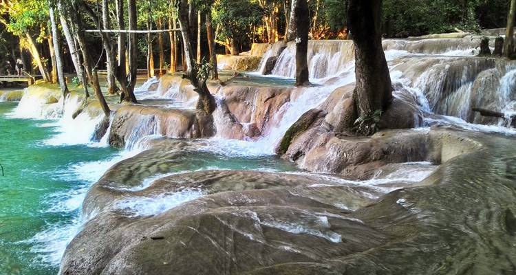 Gestufte türkisfarbene Becken fließen über glatte Kalksteinterrassen tief im Dschungel der Kuang Si Wasserfälle.