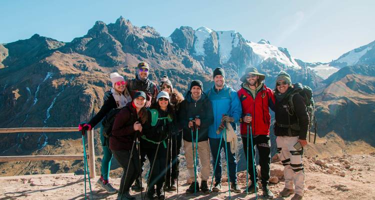 Happy trekking group with poles pose before dramatic glaciated peaks on a sunny Andean morning.
