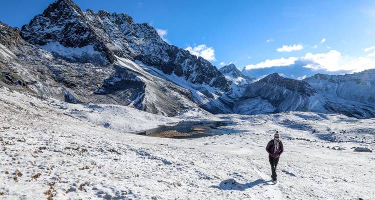 Solo trekker walks across snowy alpine landscape with jagged black mountain looming above.