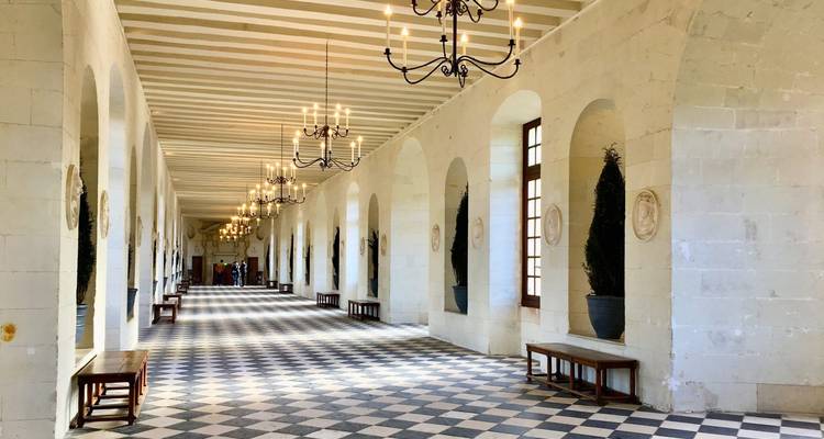 Long arched interior corridor with chandeliers and black-and-white checkered floor at Château de Chenonceau.