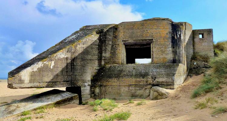 World War II concrete bunker partially buried in sand dunes under a blue sky at Omaha Beach.
