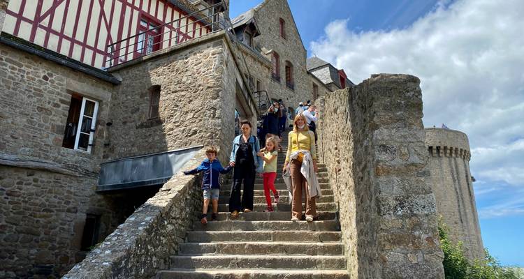 Family descends ancient stone steps within the ramparts of Mont Saint-Michel under blue skies.