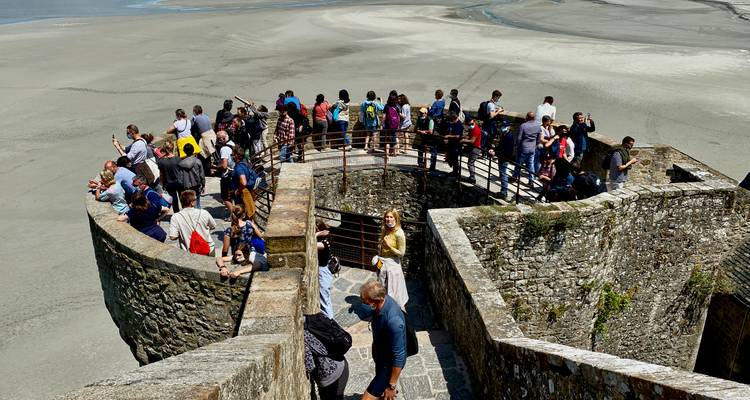 Large crowd gathers on a stone bastion overlooking expansive tidal flats at Mont Saint-Michel.