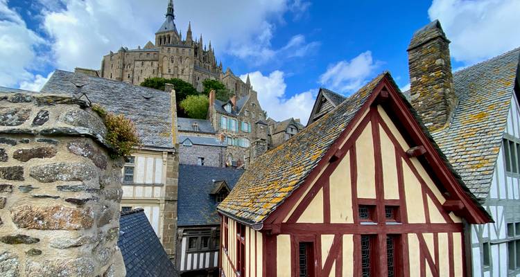 Schilderachtig uitzicht op middeleeuwse stenen en houten daken die leiden naar de beroemde abdij die bovenop de Mont Saint-Michel staat onder een heldere blauwe hemel.