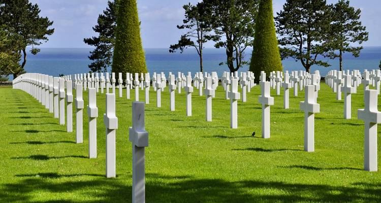 Eindeloze rijen witte kruisen in het verzorgde Normandy American Cemetery tegen een achtergrond van blauwe zee.