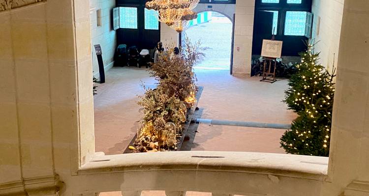 Interior hall of a Loire château with chandelier, seasonal floral display and a view to the courtyard.