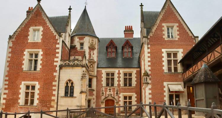 Brick and stone Renaissance manor house with steep slate roofs and ornate chimneys on an overcast day.