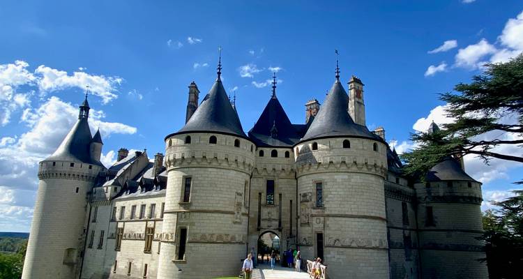 Fairy-tale turrets of Château de Chaumont-sur-Loire rise against a vivid blue sky while visitors approach the entrance bridge.