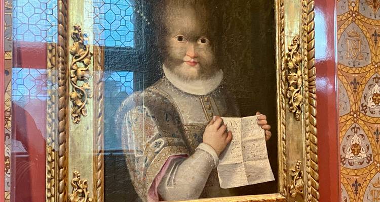 Close-up of a framed Renaissance portrait painting displayed on a patterned red wall.