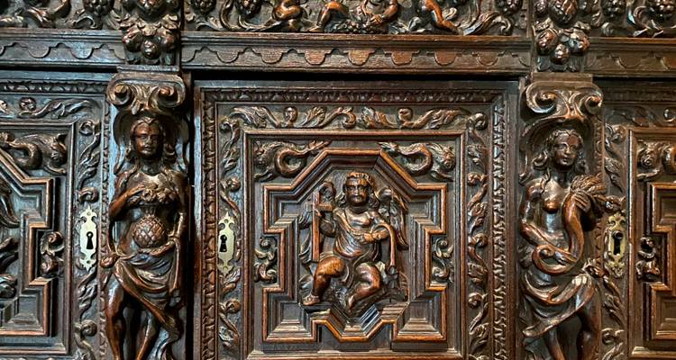 Highly detailed carved wooden cabinet panels featuring cherubs and mythological figures.