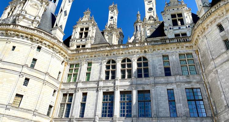Upward angle of Château de Chambord’s ornate rooftop spires and dormer windows against a vivid blue sky.