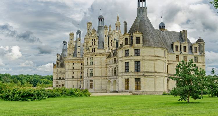 Wide lawn leading to the stately towers and lantern-capped roofs of Château de Chambord under a brooding sky.