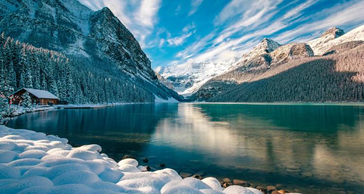 Snow-covered Lake Louise with turquoise water reflecting dramatic Rocky Mountain peaks under a brilliant winter sky.