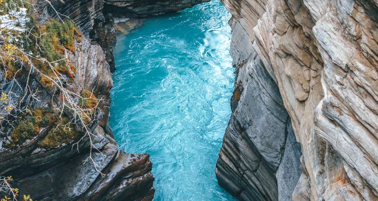 Agua turquesa se precipita a través de un estrecho cañón rocoso con paredes de piedra en capas y cornisas musgosas