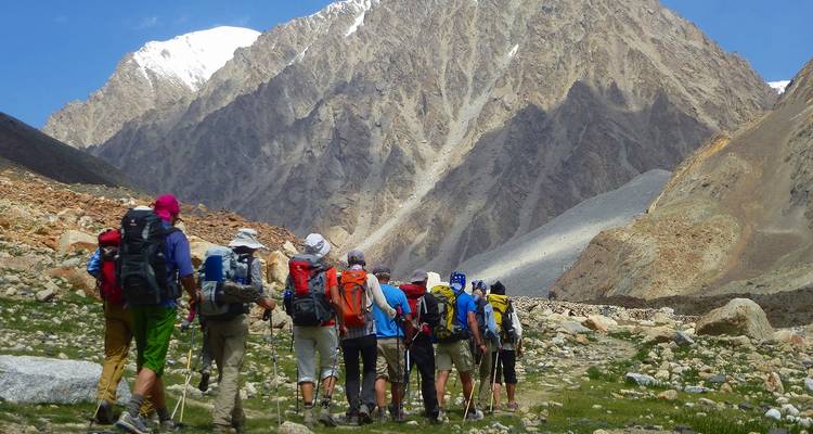 Fila de excursionistas con mochilas caminando por un valle alpino rocoso hacia imponentes picos escarpados.