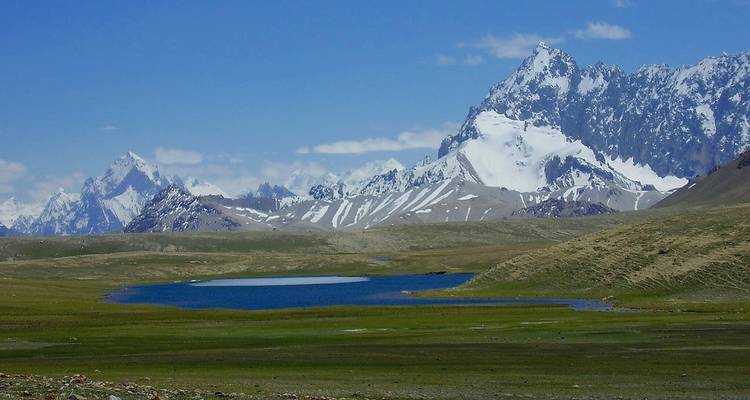 Lago alpino tranquilo situado en una vasta meseta herbosa con dramáticas agujas cubiertas de nieve alrededor.