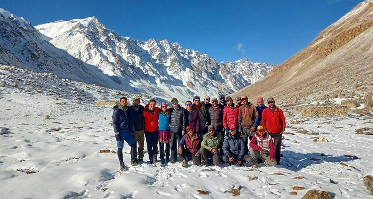 Grupo de senderismo sonriendo en valle nevado del Himalaya rodeado de picos escarpados bajo sol brillante.