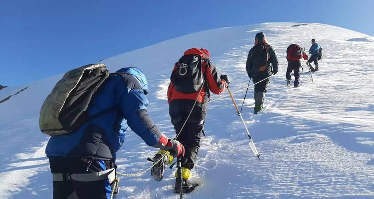 Escaladores ascendiendo por una pendiente empinada de nieve usando piolets y cuerda bajo un cielo azul brillante.
