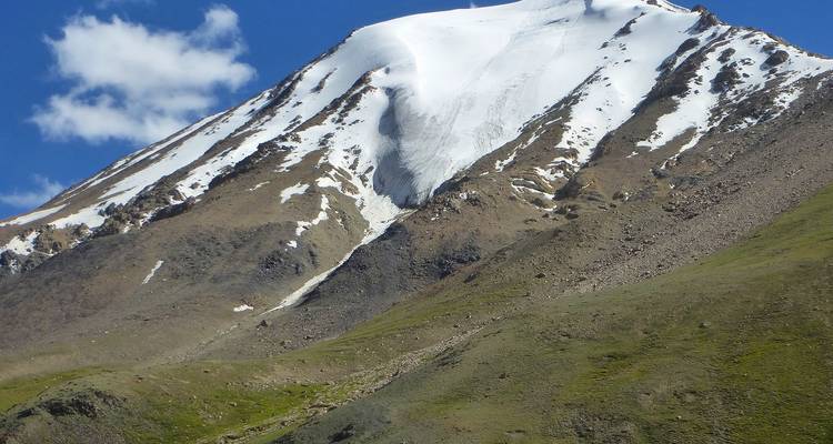 Pico de montaña aislado cubierto de nieve bajo un cielo azul profundo que se eleva sobre laderas cubiertas de hierba.