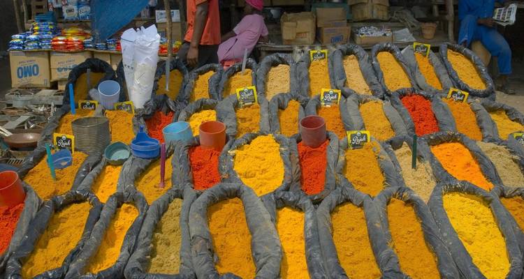 Colorful open-air market stall displaying rows of vivid ground spices in black plastic troughs.