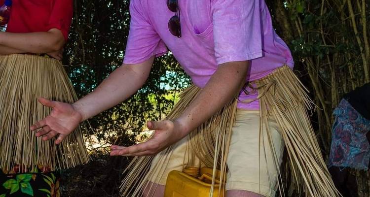 Close-up of traveller wearing a pink shirt and grass skirt performing a traditional dance gesture among bamboo trees.