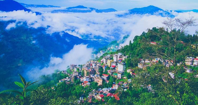 Panoramic view of a mist-filled valley and colourful hillside town surrounded by blue mountains.