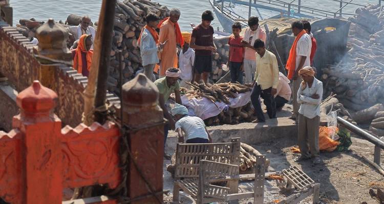 Les gens se rassemblent autour d'un bûcher funéraire sur les ghats de pierre au bord de la rivière.