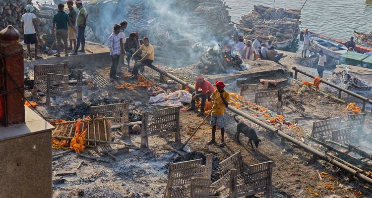 Lieu de crémation enfumé au bord de la rivière avec des ouvriers s'occupant des feux et des tas de bois.