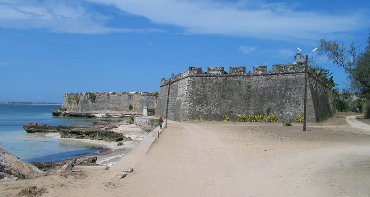 Historic stone coastal fortress with crenellated walls stretching along turquoise shallows under a clear blue sky.