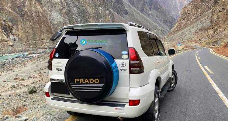 Toyota Prado blanco estacionado en una carretera serpenteante de montaña junto a un desfiladero de río.