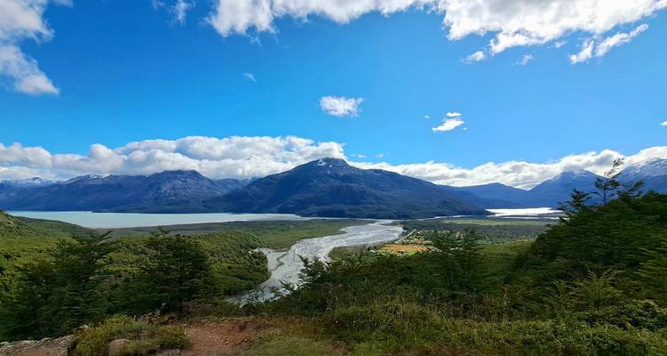 Vista panorámica patagónica de ríos entrelazados, lagos esmeralda y montañas boscosas bajo un cielo brillante.