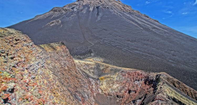 Steep cone of Pico do Fogo volcano with colorful volcanic rocks and clear blue sky.