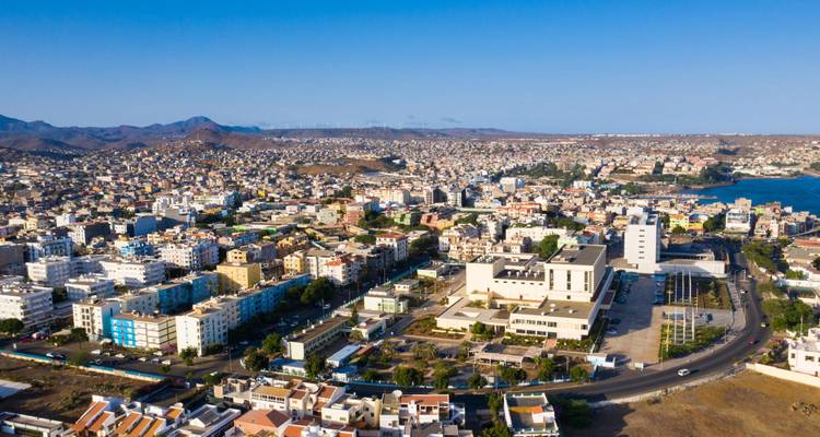 Aerial panorama of a coastal city packed with buildings, with hills and a blue bay visible on a clear day.