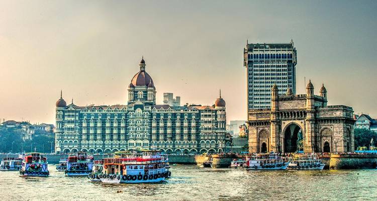 Taj Mahal Palace Hotel und Gateway of India Bogen vom Hafen aus betrachtet mit bunten Fähren.