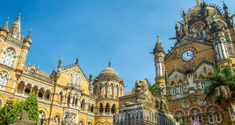 Ornater gotisch-viktorianischer Chhatrapati Shivaji Terminus vor strahlend blauem Himmel mit steinerner Löwenstatue.