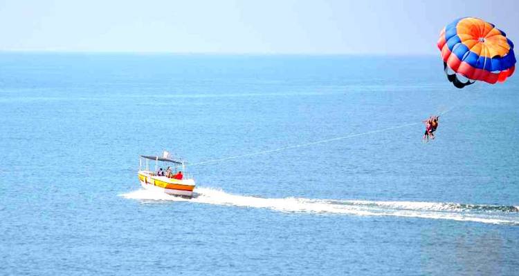 Heller Parasail hebt zwei Personen über das blaue Arabische Meer, während ein Speedboot sie zieht.