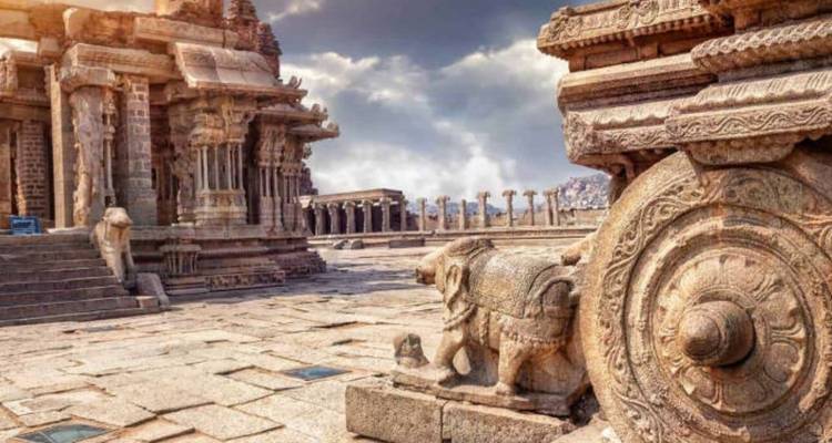 Antike Steinwagen- und Elefantenschnitzereien inmitten einer Tempelruinenanlage unter dramatischem Himmel in Hampi.