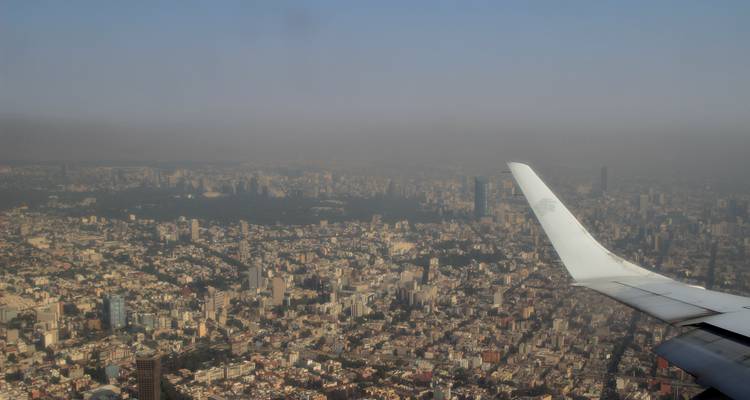 Aile d'avion au-dessus d'une vaste métropole brumeuse s'étendant jusqu'aux collines lointaines.
