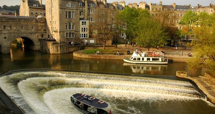 Vue panoramique du pont Pulteney et du déversoir en arc avec des bateaux touristiques sur la rivière Avon bordée d'architecture géorgienne et d'arbres printaniers
