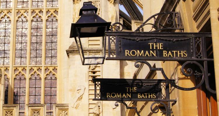 Enseigne ornée en fer forgé indiquant 'The Roman Baths' suspendue à l'extérieur d'un bâtiment en pierre gothique