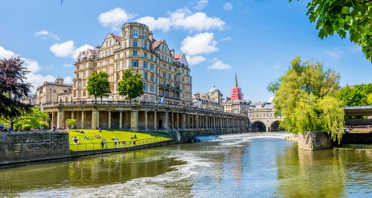 Colonnade élégante au bord de la rivière et bâtiments historiques reflétés dans l'eau calme sous un ciel bleu éclatant