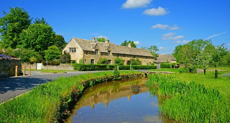 Scène rurale tranquille avec des cottages en pierre se reflétant dans un ruisseau étroit bordé d'une végétation printanière luxuriante
